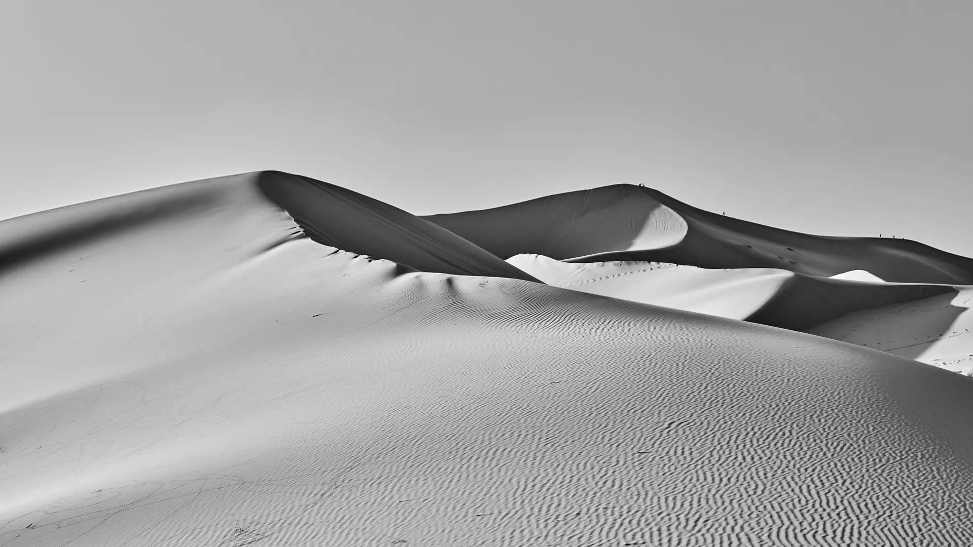 Black and white minimalist photograph of sculpted desert sand dunes with sharp ridgelines, Merzouga, Sahara Desert, Morocco