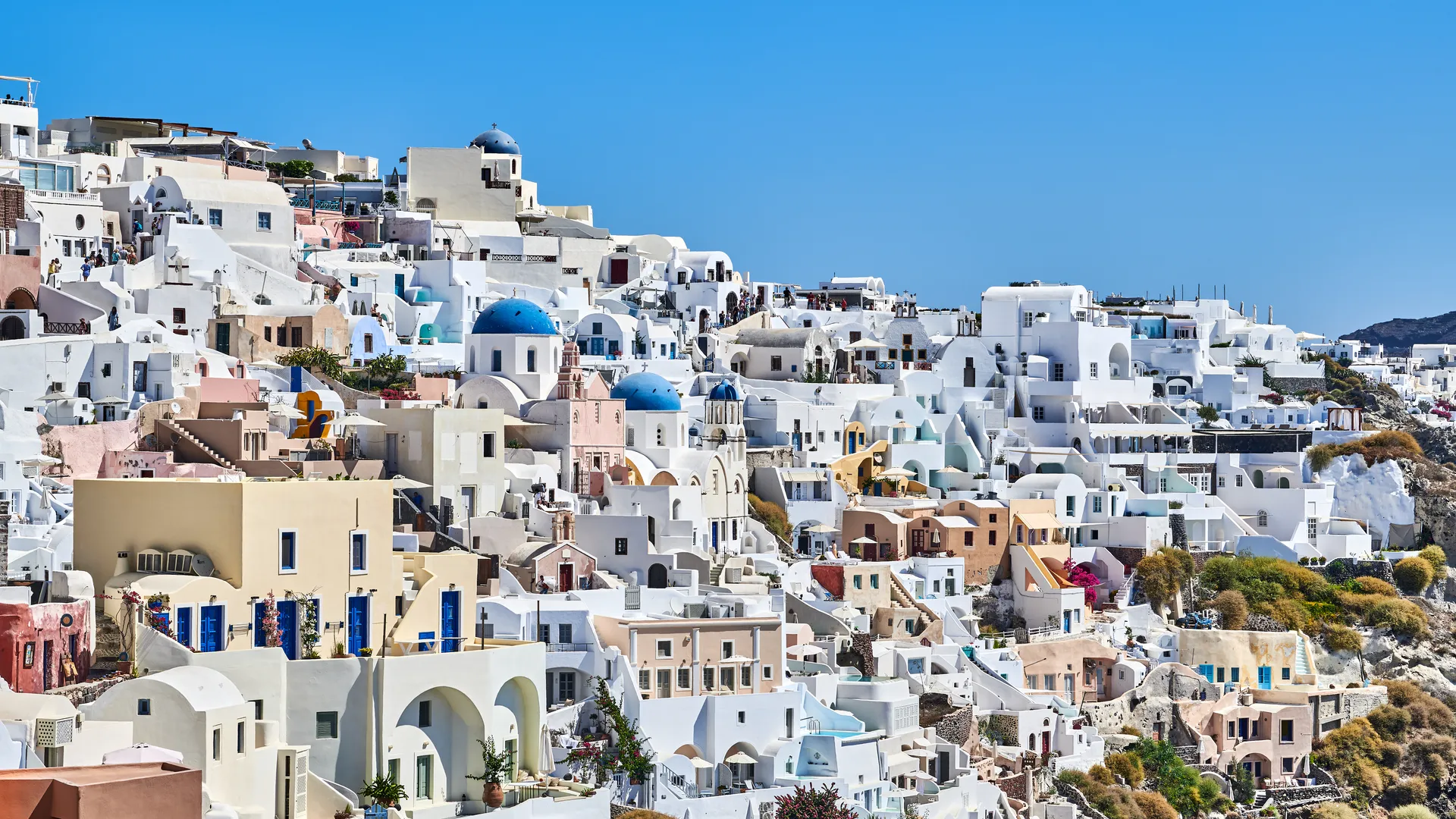 White-washed buildings with blue domes cascading down a hillside in Santorini, Greece