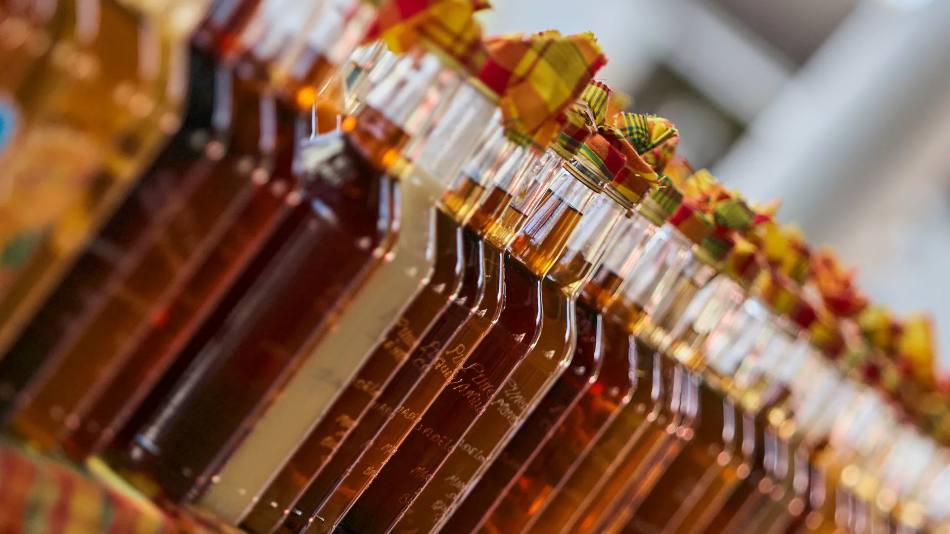 Rows of artisanal rum bottles with colorful Madras fabric tops at a Caribbean market, Guadeloupe Island, France